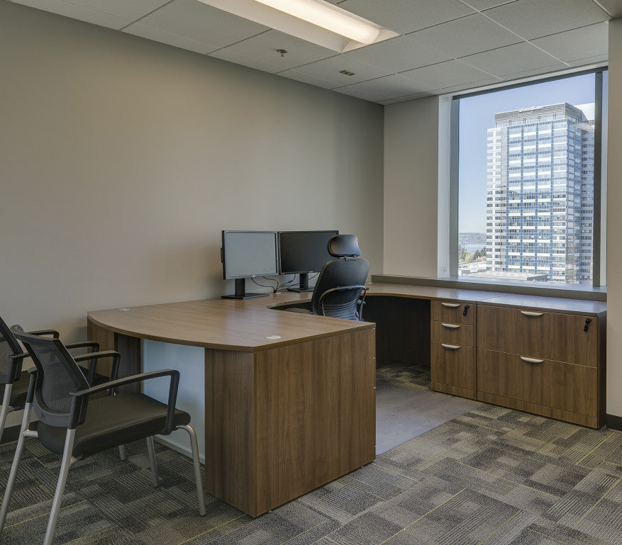 A private office with a wood desk, credenza and guest chairs